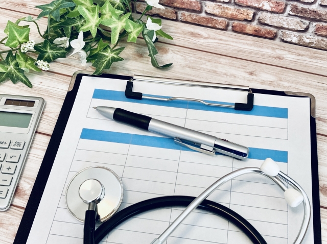 白い木目の机の上に置かれた聴診器と問診票